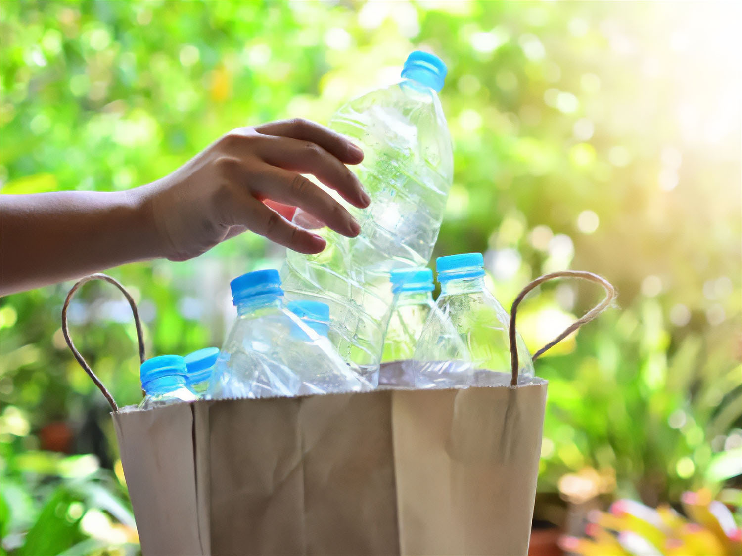 Hand placing empty plastic bottles into a paper bag